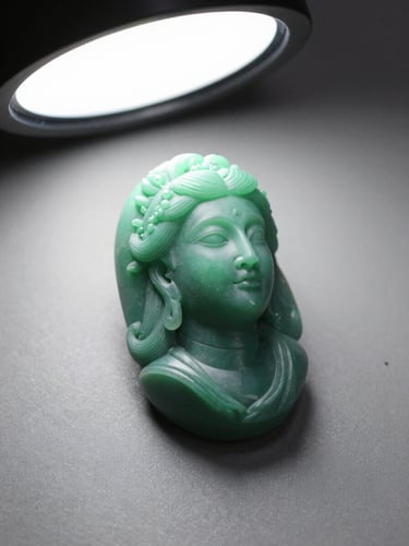 Three-quarter view of a carved green jewellery wax model on a neutral matte grey surface, cool overhead studio strobe lighting, crisp shadow on one side revealing the three-dimensional form, no hands or tools in frame