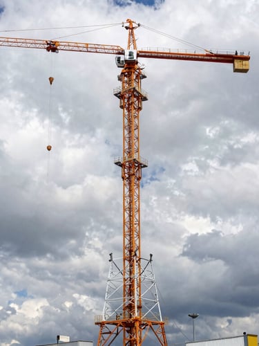 Wide-angle industrial engineering photography of a massive telecommunication tower being assembled by cranes under a dramatic cloudy Andean sky, safety orange accents on equipment.