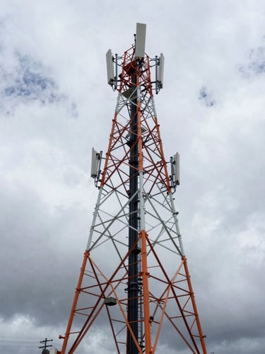 Wide-angle industrial engineering photography of a massive telecommunications tower against dramatic overcast Andean skies, high-contrast cool steel tones with subtle safety orange accents.