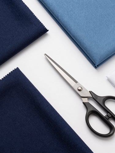Crisp studio product photography, bright neutral lighting, flat-lay of premium fabric swatches in navy, steel blue, and white, neatly arranged with tailoring scissors, sharp focus
