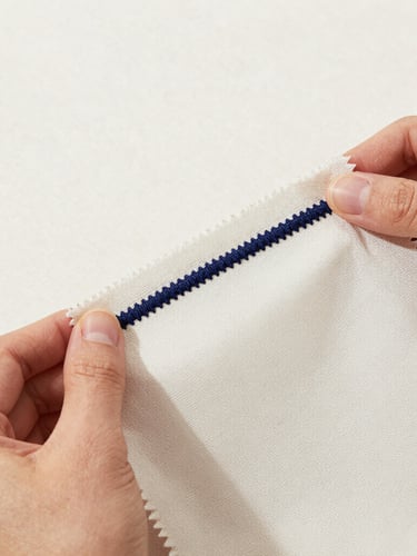 Crisp studio product photography of hands holding a physical fabric swatch with precise navy embroidery, bright neutral lighting, detailed fabric textures, sharp focus