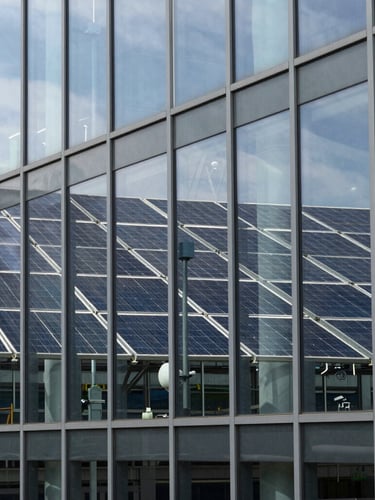 Crisp architectural close-up of a modern research facility glass facade reflecting a clean energy array, cool daylight, sharp focus