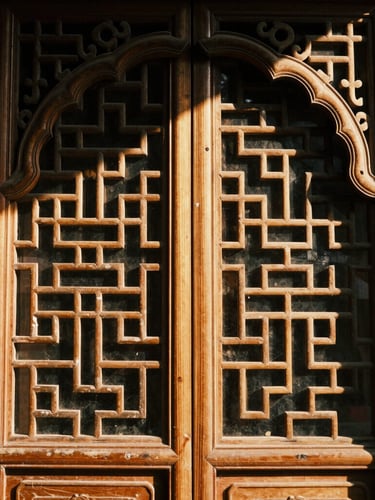 Dignified close-up of traditional carved wooden archway, warm golden-hour sunlight filtering through intricate geometric patterns, rich deep tones, 35mm.