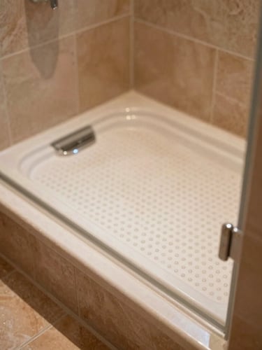 Close-up of a luxurious level-access walk-in shower tray with textured non-slip surface, warm terracotta tiles, soft natural morning daylight, 35mm photography