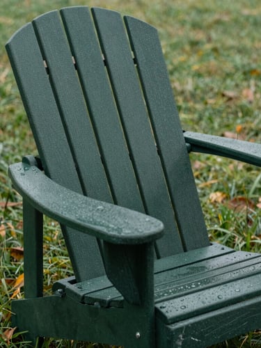 Close-up of a dark forest green Adirondack chair on a dew-covered lawn, overcast natural daylight, showing thick material texture and rugged construction