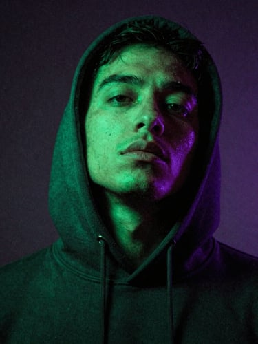 Gritty close-up portrait of SergioMdrz wearing a dark hoodie, low-angle shot, neon green gel light hitting his face, dark shadows, motion blur, 35mm film