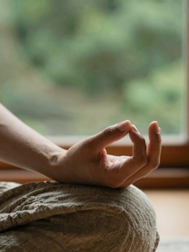 Unposed close-up of hands in a traditional mudra during meditation, warm natural window light, organic linen textures, forest green background, shallow depth of field