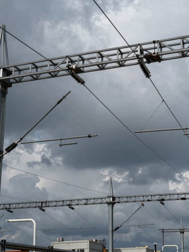 High-voltage railway overhead power line equipment, dramatic overcast sky, industrial steel gantries, sharp focus, 35mm lens.