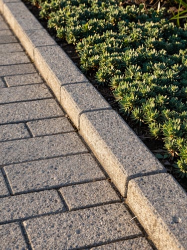 Close-up of a freshly laid coastal hardscape edge—cut pavers meeting a planted border of low salt-tolerant groundcover, afternoon light raking across the stone surface showing texture and precision