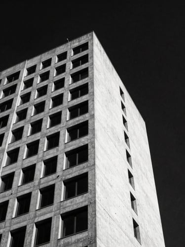 Low-angle stark monochrome shot of a brutalist concrete skyscraper corner cutting into a dark obsidian sky, sharp shadows, high contrast, 35mm film
