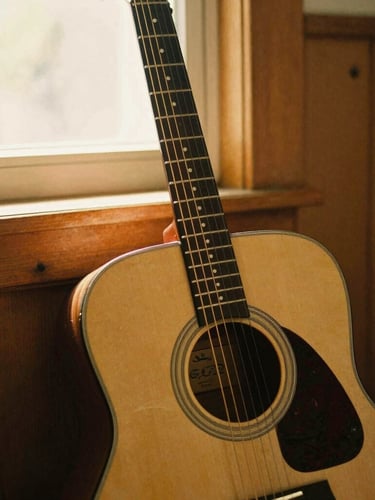 Intimate medium shot of an acoustic guitar leaning against a wooden wall, soft golden light filtering through a window, warm sepia tones, 35mm film style