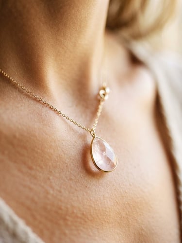 Macro shot of a delicate gold necklace with a luminous rose quartz pendant catching soft morning daylight on warm skin, shallow depth of field