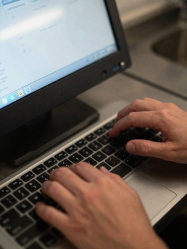 Extreme close-up overhead shot of hands entering data into a kitchen order terminal, dimly lit by screen glow and fluorescent overhead light, stainless steel prep surface visible below the keyboard, motion blur on fingers mid-keystroke