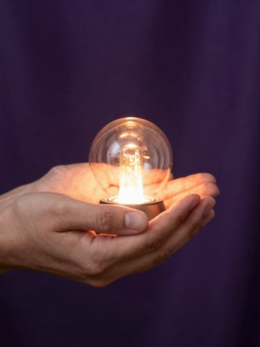 Vertical portrait frame. Close-up of hands gently holding a small, glowing warm light source against a soft dark violet fabric background, representing technology holding sacred energy.