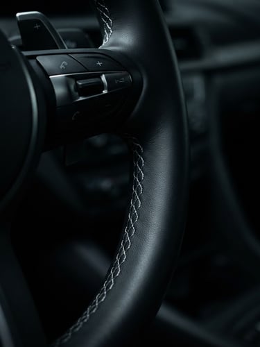Macro close-up of a pristine leather steering wheel with precise silver stitching, low-key dramatic studio lighting casting deep shadows on the dashboard, 50mm lens.