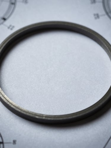 Industrial macro photography of a reinforced composite gasket laid flat on a technical blueprint schematic, cool metallic tones, sharp focus, 50mm