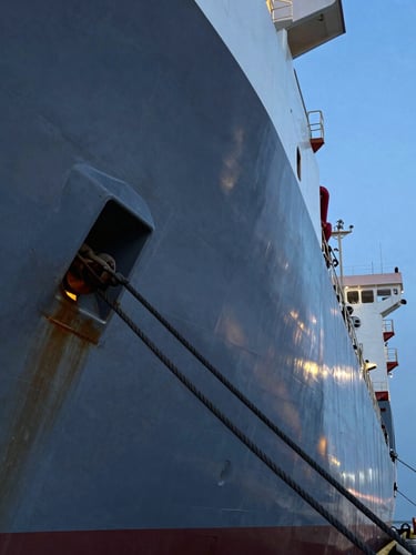 Extreme close-up of a heavy steel hull and mooring lines of a platform supply vessel docked at an industrial port, cold blue hour lighting