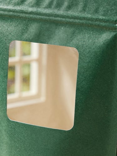 Macro close-up of folded forest green packaging prototypes showing clean custom die-cuts, natural side-lit window daylight, high texture detail.