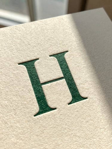 Macro shot of a heavy-weight textured cotton paper card with crisp debossed serif typography, natural side-lit window daylight casting soft shadows, warm cream tone.