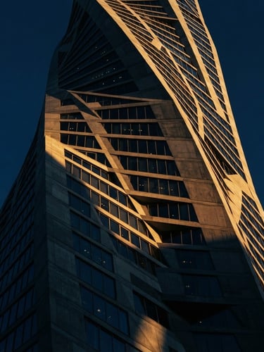 Dramatic low-key architectural photography of a soaring concrete and glass skyscraper facade in Dubai, golden hour sunlight casting sharp geometric shadows, rich navy tones, 35mm