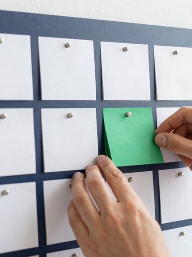 Close-up of hands organizing a physical Kanban board with clean notes, bright natural daylight, modern workspace