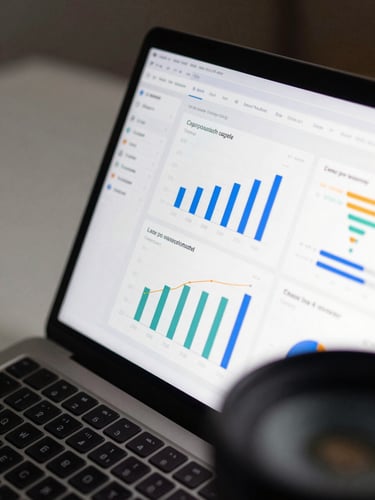 Close overhead detail of a laptop screen displaying a clean analytics dashboard with data visualizations — bar charts and funnel metrics — on a matte desk surface, cool studio lighting from the left, no person visible, tight crop showing only the screen and keyboard edge