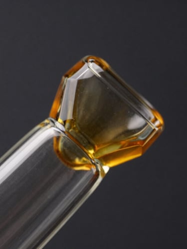 Macro close-up of geometric hand-blown glass pipe, clean lines, dark charcoal background, warm amber accent lighting, sharp focus, high contrast