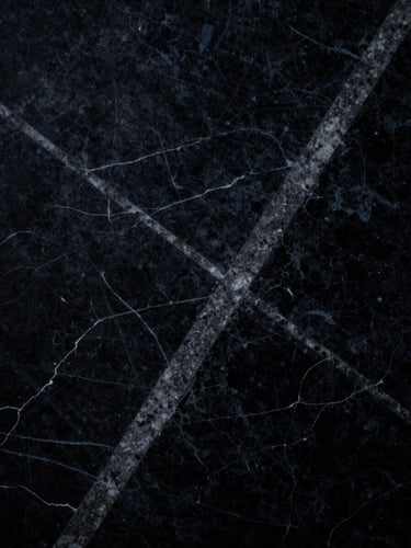 Macro close-up of a dark textured marble slab with sharp geometric veins, dramatic low-key lighting, high-contrast shadows, 35mm