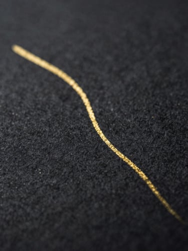 Macro close-up of dark charcoal paper texture with a single fine-line gold ink stroke, dramatic low-key lighting, 35mm