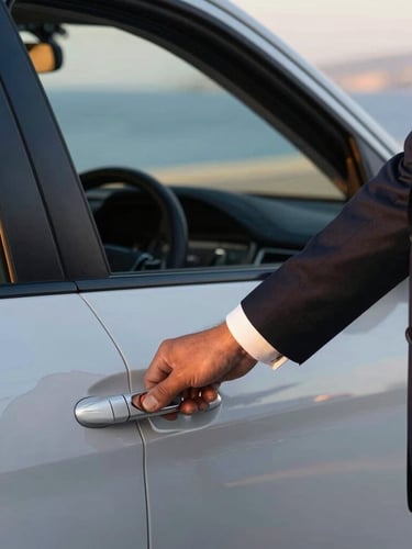 Close-up of a professional driver in a dark suit opening a polished vehicle door, crisp white shirt cuffs, soft golden-hour Aegean light, shallow depth of field.