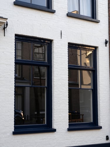 A beautifully restored historic white brick residential facade in Den Haag with glossy dark navy painted window frames reflecting the morning sun, clean lines