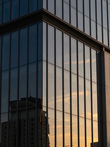 Dramatic golden-hour architectural light reflecting on a modern glass facade in Dammam, clean corporate lines, 35mm lens.