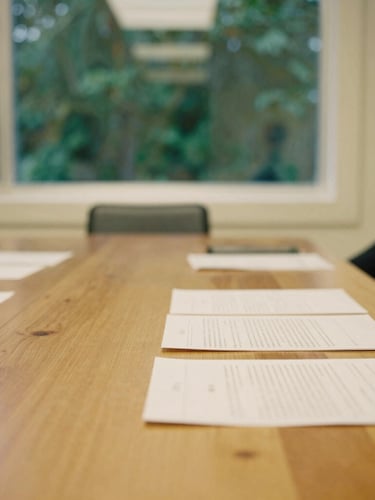 A warm collaborative session in a light-filled California boardroom, physical documents on a wooden table, soft window light, shallow depth of field, 35mm