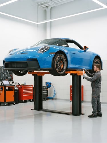 Spotless, brightly lit modern automotive service bay with clean white floors, a vehicle elevated on a hydraulic lift, and high-visibility safety orange accents, sharp focus, 35mm