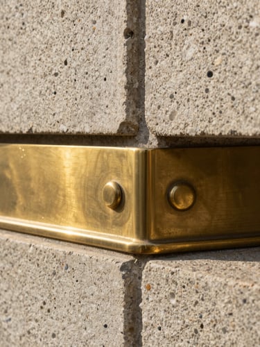 Portrait crop of a brushed brass architectural joint meeting raw textured stone, indirect morning light emphasizing the physical materials