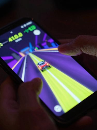 Extreme close-up dynamic angled shot of a high-fidelity Android phone displaying a fast-paced neon racing game, vibrant cyber lime and violet screen-glow casting onto a hand, dark moody ambient background, shallow depth of field.