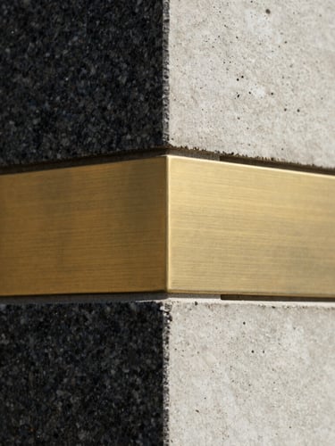 Extreme close-up of premium textured raw materials, dark granite, brushed brass, and cast concrete meeting at a sharp geometric angle, dramatic architectural lighting