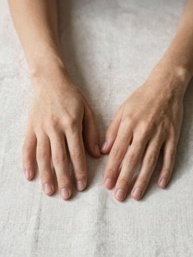 Close-up of hands resting on a clean light linen surface, soft natural daylight, minimalist composition, 35mm lens.