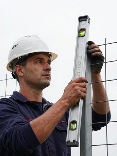 Close-up portrait, low-angle, of a skilled Perimix Fence builder, wearing a hard hat, meticulously checking the vertical alignment of a freshly set fence post with a long, professional level tool. High-contrast, sharp focus, overcast daylight, emphasizing precision and craftsmanship.
