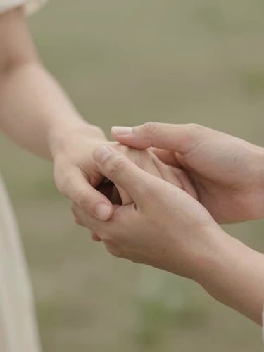 Warm editorial photography of soft diffused daylight falling on two hands gently holding each other, warm cream and sage tones, gentle focus, shallow depth of field, peaceful sanctuary atmosphere.