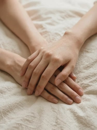 A close-up of two hands gently resting together on a soft cream linen sheet, bathed in warm, diffused morning light, expressing comfort and companionship.