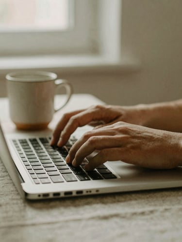 Intimate close-up of hands typing on a laptop next to a warm ceramic mug on a linen tablecloth, soft natural window light, muted sage and beige tones