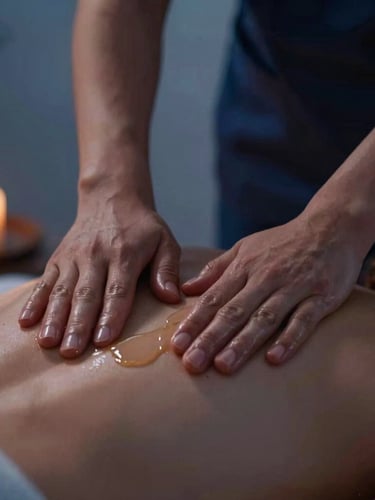 Close-up macro shot of professional therapist's hands applying warm natural massage oil to a client's back, focus on the hands and oil, soft diffused twilight lighting, warm editorial photography, deep indigo and warm sand tones, shallow depth of field, 35mm