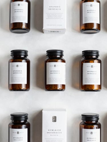 A crisp flat-lay of premium packaged wellness and Ayurvedic skincare goods in structured amber glass jars and minimalist white boxes, bright natural light, top-down perspective.