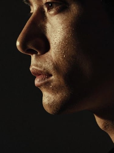 Dramatic chiaroscuro macro portrait of a man's sharp jawline and profile, low-key studio lighting, deep shadows, brushed gold undertones, 35mm.