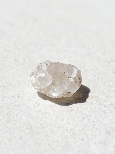 A close-up of pure raw mineral crystals on a textured white stone surface, bright natural daylight, sharp focus, 50mm lens, minimalist slate tones