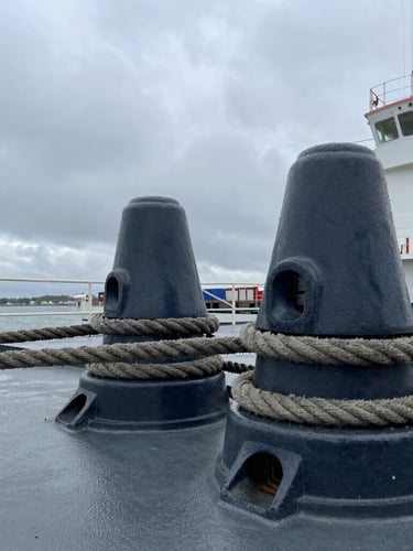Close-up of heavy-duty steel marine hardware and mooring ropes on a cargo ship deck, overcast harbor lighting, sharp industrial detail.
