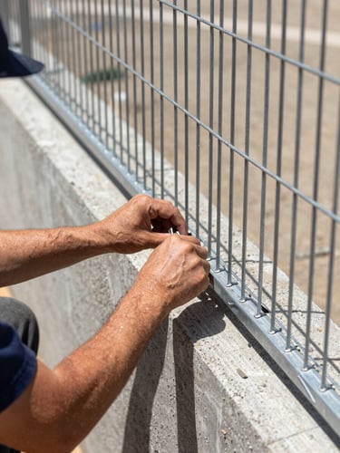 Close-up of a technician's hands installing heavy-gauge steel mesh exclusion barriers along a concrete foundation, bright California daylight, sharp focus, 35mm lens