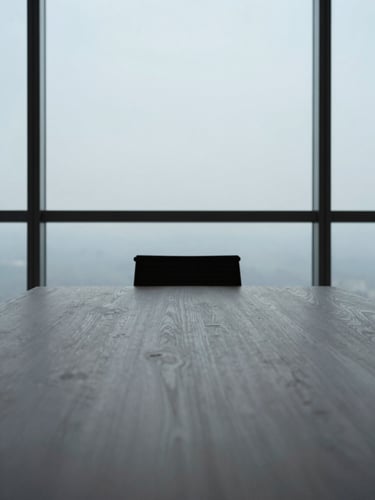 Close-up, wide-angle architectural photograph of a minimalist, high-end boardroom table with a single chair, natural light streaming from a large window, conveying quiet authority and focused intent.