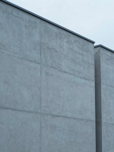 Minimalist architectural detail of a modern concrete facade with clean geometric lines, cast in overcast morning light with desaturated blue tones, 35mm lens.